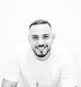 A bright, minimalist portrait of Muneeb Ahmed smiling confidently against a clean, colorful background.