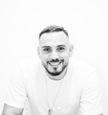 A man smiling while wearing a clean, modern t-shirt with a subtle inspirational message, standing against a neutral background.
