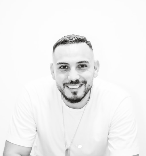 A bright, minimalist portrait of Muneeb Ahmed smiling confidently against a clean, colorful background.
