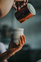 A close-up of hands pouring Zamzam water into a delicate glass cup.