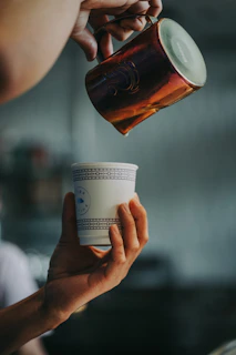 A close-up of hands pouring Zamzam water into a delicate glass cup.