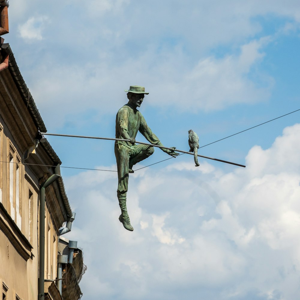 una estatua de un hombre que se balancea sobre una cuerda floja con un pájaro posado