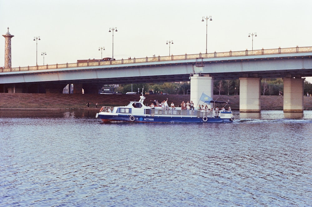 a blue and white boat traveling under a bridge