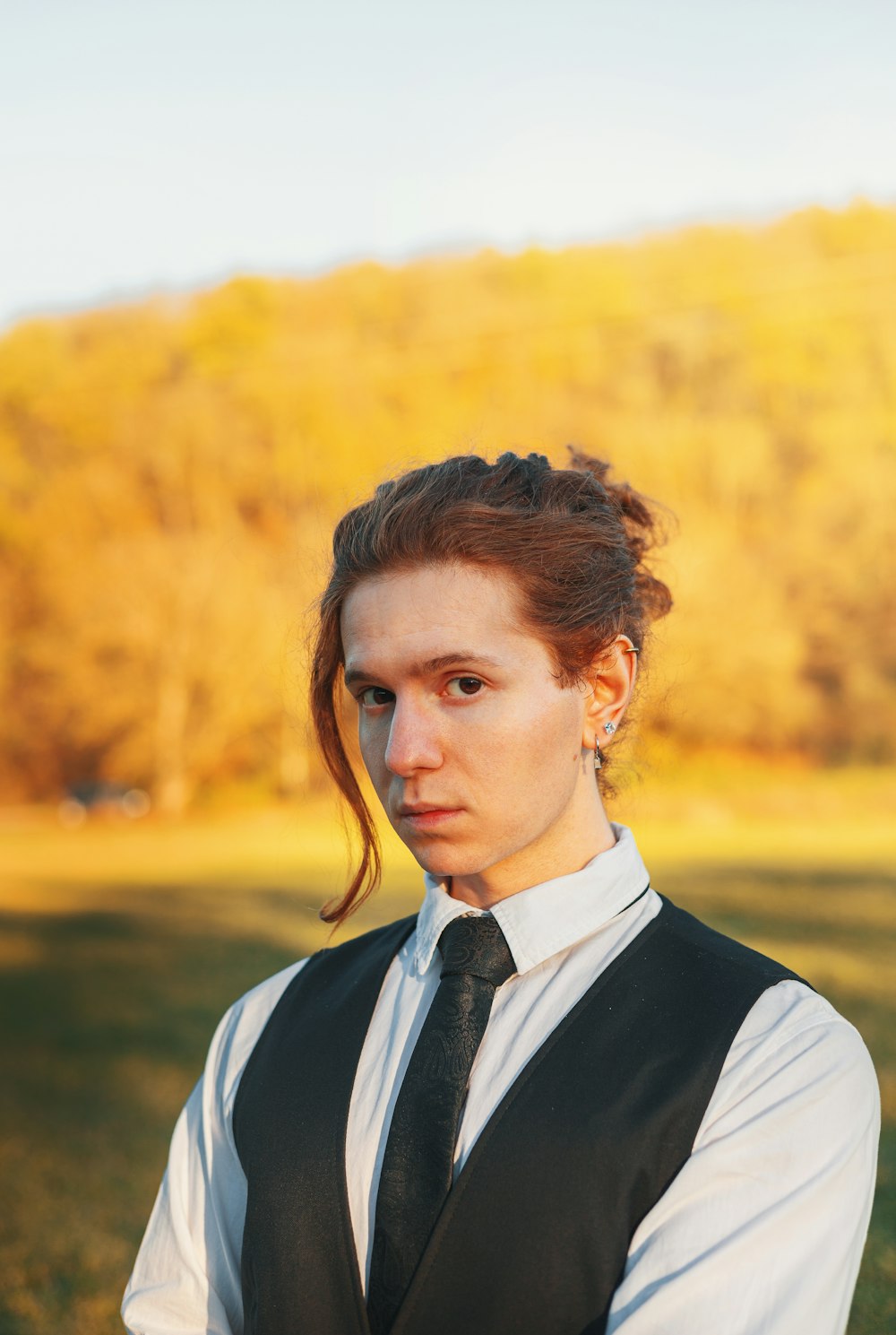 a woman wearing a vest and tie standing in a field