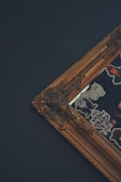 A detailed image of an ornate, vintage-style picture frame with intricate designs. The frame corner is decorated with embellishments, and there are various stickers with different designs on the reflective surface inside the frame.