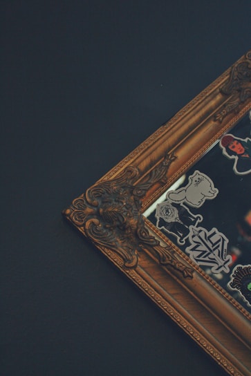 A detailed image of an ornate, vintage-style picture frame with intricate designs. The frame corner is decorated with embellishments, and there are various stickers with different designs on the reflective surface inside the frame.