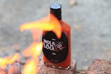 A bottle of hot sauce labeled 'Hola Loca' is placed on bricks with flames in the foreground, creating a dynamic scene.