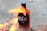 A bottle of hot sauce labeled 'Hola Loca' is placed on bricks with flames in the foreground, creating a dynamic scene.