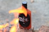 A bottle of hot sauce labeled 'Hola Loca' is placed on bricks with flames in the foreground, creating a dynamic scene.