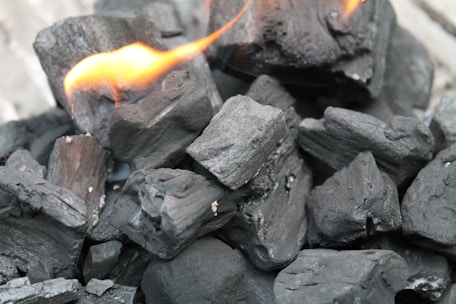 A close-up view of several pieces of black charcoal, some of which have small flames burning on them.