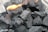 A close-up view of several pieces of black charcoal, some of which have small flames burning on them.