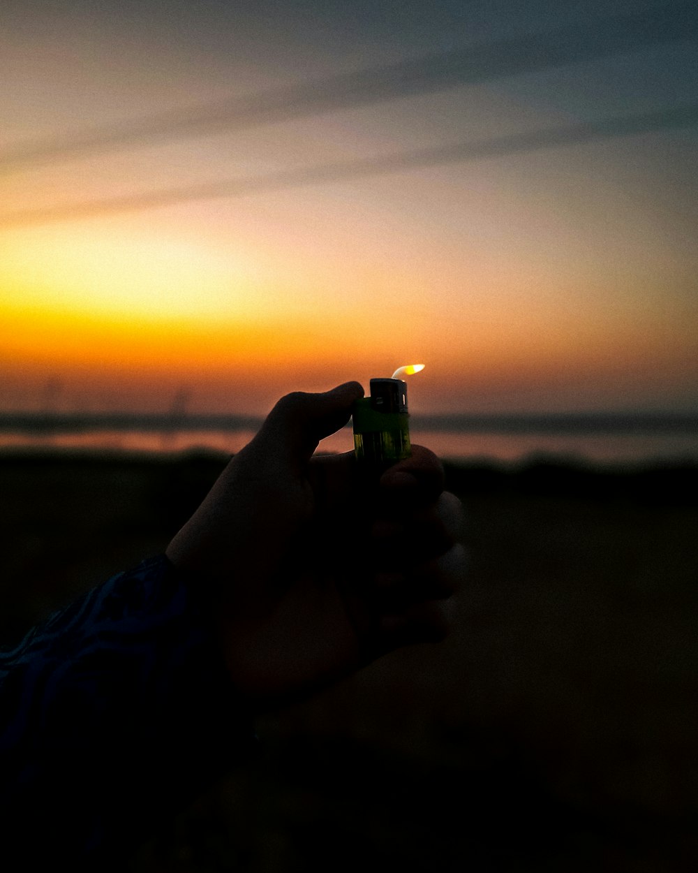 a person holding a lighter in front of a sunset