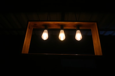 Three light bulbs are mounted in a horizontal wooden frame against a dark background. The bulbs emit a warm glow, creating a cozy atmosphere.