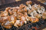 Pieces of marinated chicken are arranged on a barbecue grill, cooking over hot coals. The seasoning appears to be a mixture of herbs and spices, giving the chicken a rich, appetizing appearance.