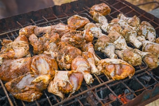 Pieces of marinated chicken are arranged on a barbecue grill, cooking over hot coals. The seasoning appears to be a mixture of herbs and spices, giving the chicken a rich, appetizing appearance.