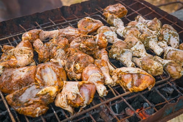 Pieces of marinated chicken are arranged on a barbecue grill, cooking over hot coals. The seasoning appears to be a mixture of herbs and spices, giving the chicken a rich, appetizing appearance.