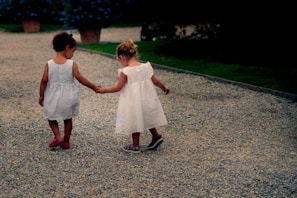 Two sisters walking barefoot on a soft earth path, holding hands