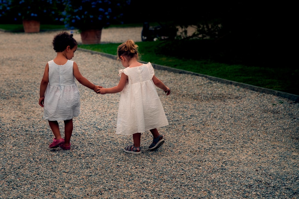 two little girls holding hands walking down a gravel path