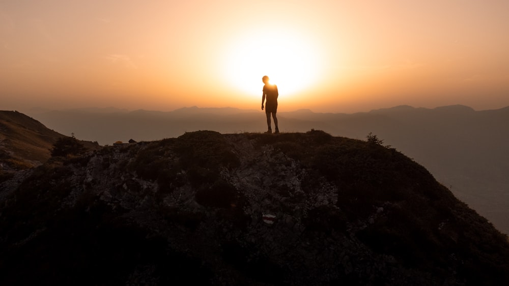 un homme debout au sommet d’une montagne au coucher du soleil