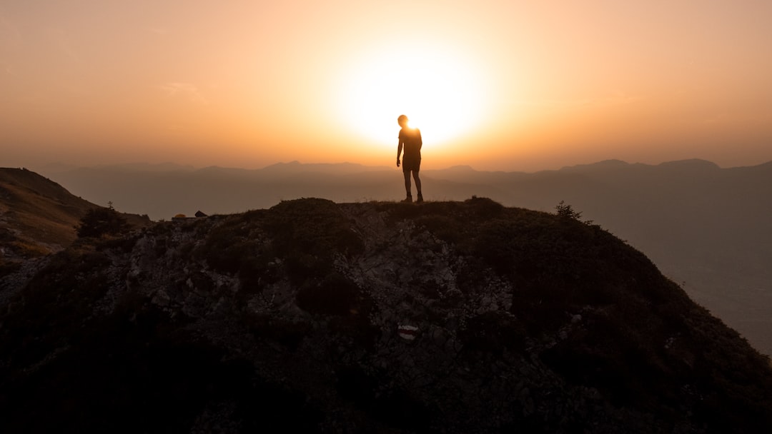 a man standing on top of a mountain at sunset, Man standing alone on a ridge in the Swiss mountains watching the sunset.