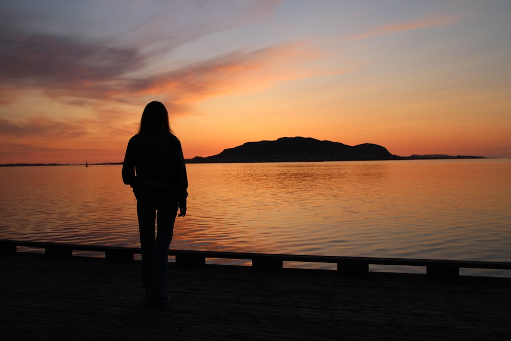 a person standing on a dock watching the sunset