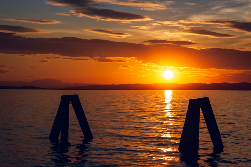 a sunset over a body of water with wooden posts sticking out of the water