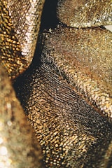 An up-close view of shimmering, textured gold fabric with a reflective and intricate pattern, creating a luxurious appearance.