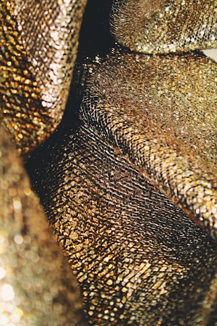 An up-close view of shimmering, textured gold fabric with a reflective and intricate pattern, creating a luxurious appearance.