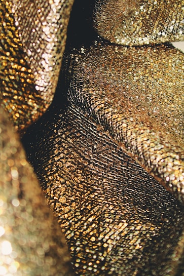 An up-close view of shimmering, textured gold fabric with a reflective and intricate pattern, creating a luxurious appearance.