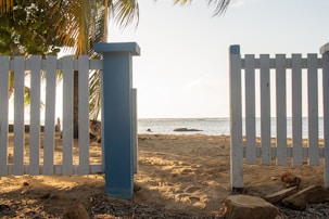 A technician inspecting a white picket fence under bright sunlight near a beach house.