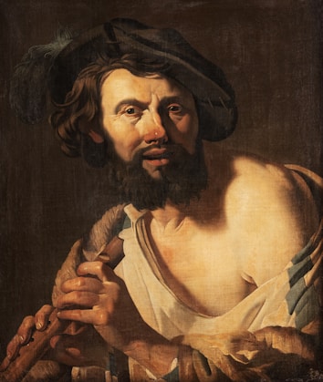 A man with a beard and wavy hair is wearing a feathered cap and a partially draped garment. He is playing a musical instrument, which appears to be a flute. The lighting is dramatic, highlighting his facial features and the texture of his clothing.