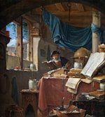 A cluttered study with an elderly man reading a book. The room is filled with various objects, including books, jars, and an astrolabe. A large open book is prominently displayed on a desk draped with a red cloth. Sunlight enters through a window with lattice work, casting shadows and illuminating the scene. A birdcage hangs by the window, and a blue curtain is draped across a column.