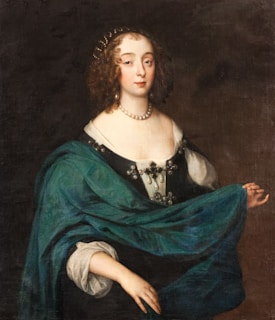 A portrait of a woman with curly brown hair adorned with a pearl headpiece. She wears a pearl necklace and an elegant black dress with a white neckline, embellished with ornate decorations. Draped over her shoulders is a luxurious teal shawl. Her expression is serene and composed, with a subtle half-smile.