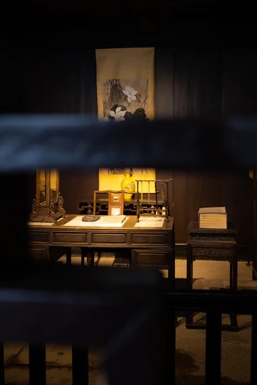 An elegant, dark-toned study desk with ancient tomes, parchment maps, and a softly glowing candle.