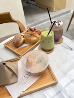 A colorful spread of pastries laid out on a rustic wooden table next to matcha and chai drinks.