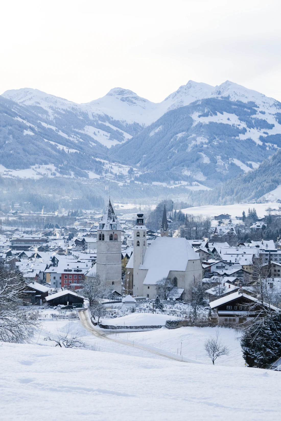Besneeuwd Kitzbühel met kerktoren en bergen op de achtergrond