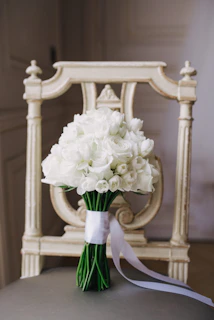 Bridal bouquet featuring white roses and baby blue ribbons resting on a vintage chair