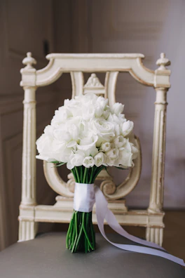 An elegant bridal bouquet featuring white roses and baby blue ribbons resting on a vintage chair.