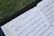 A sheet of music is open on a stand outdoors, featuring the piece 'Every Breath You Take' arranged for violoncello by Lorenzo Golofeev. The pages are held in place with rings, and the background is a blurred green, likely grass.