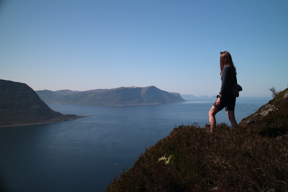 a woman standing on top of a grass covered hillside