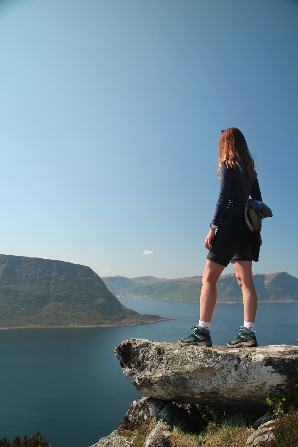 a woman standing on top of a rock next to a body of water