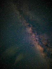 A star-filled night sky with a dense cluster of stars forming a bright band across the image, likely representing the Milky Way galaxy. The stars vary in brightness and color, set against a deep, dark background.