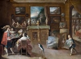 A lavishly decorated room filled with numerous paintings, sculptures, and artifacts. Several individuals are present, seemingly engaged in an art discussion. A prominently dressed man holds up a painting for others to view. A child in period costume carries another piece of artwork. The walls are adorned with framed artworks, and a table is draped with a cloth, supporting several art pieces. A parrot stands on the floor, adding to the opulent atmosphere.