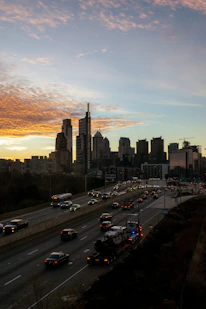 A modern cargo truck driving on a highway with a city skyline in the background.