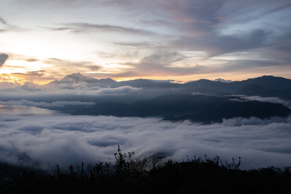 the sun is setting over the clouds in the mountains