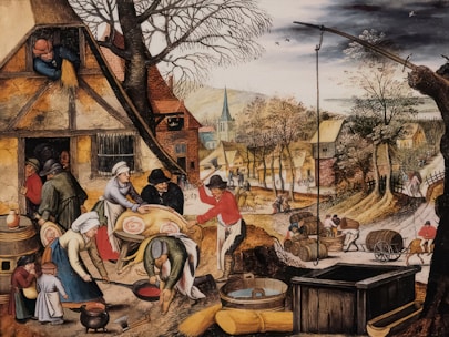 A bustling village scene featuring people engaged in various activities such as preparing food, carrying barrels, and working outside their homes. The village has rustic houses with thatched roofs, and vibrant trees line the path running through the settlement. In the foreground, several figures are preparing a large pig for cooking, while children and other adults observe and assist.