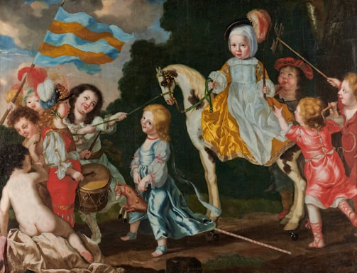 A group of children are depicted in a playful scene with one child on a horse wearing a yellow and white outfit, surrounded by others wearing colorful clothing. One child is playing a drum while another is holding a large striped flag. The scene has elements of theatrical costuming, with feathers and bright fabrics. The background includes a lush, dark green foliage.