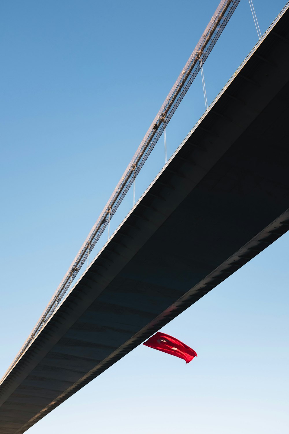 a red kite is flying under a bridge