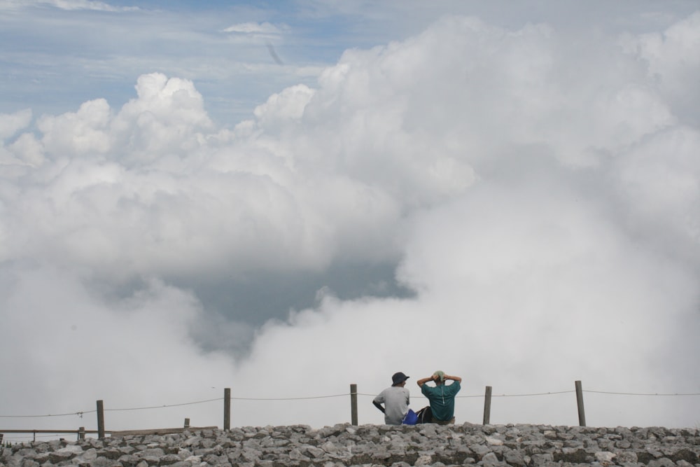 a couple of people sitting on top of a stone wall