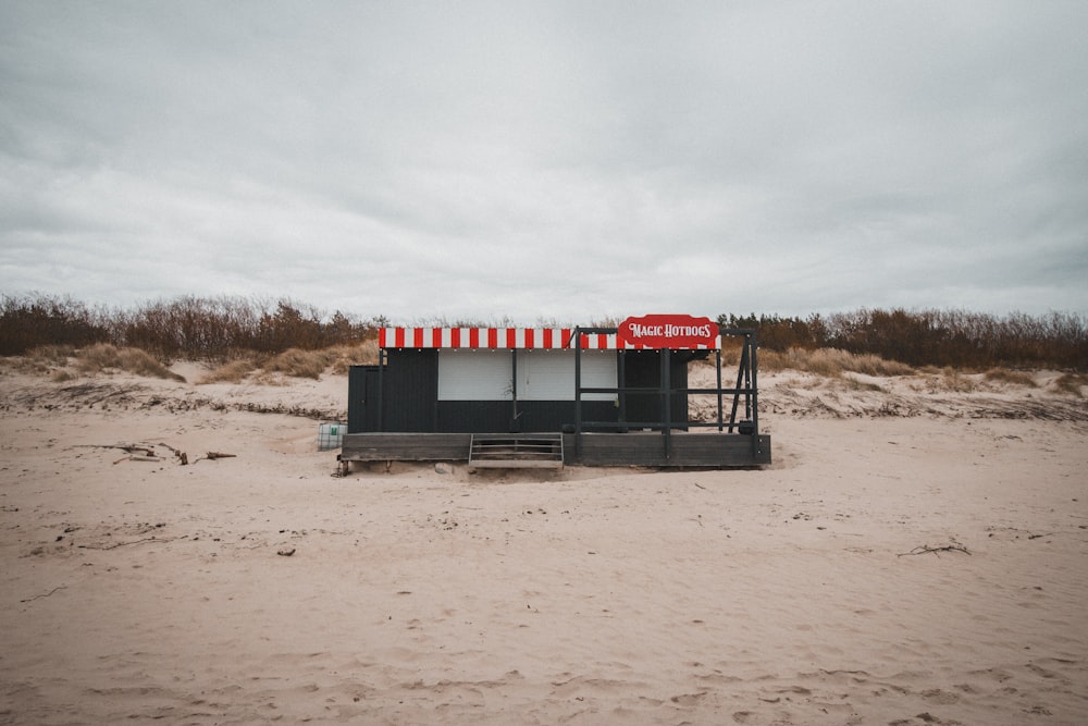 a red and white striped kiosk on a sandy beach